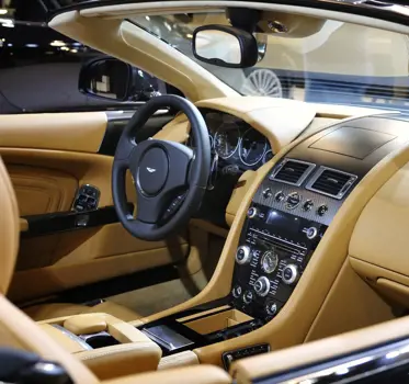 Beige leather interior of Aston Martin car, showing steering wheel, dash, and centre console