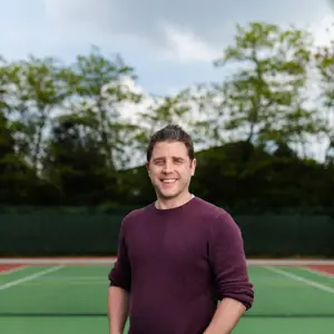 James, male sports engineer, smiles at camera on a tennis court