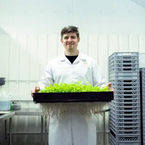 Ben Crowther, male design engineer, smiles at the camera while holding freshly grown lettuce