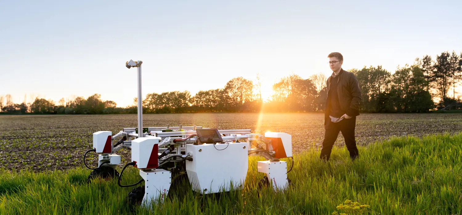 Male mechanical engineer with sustainable agricultural robot in field