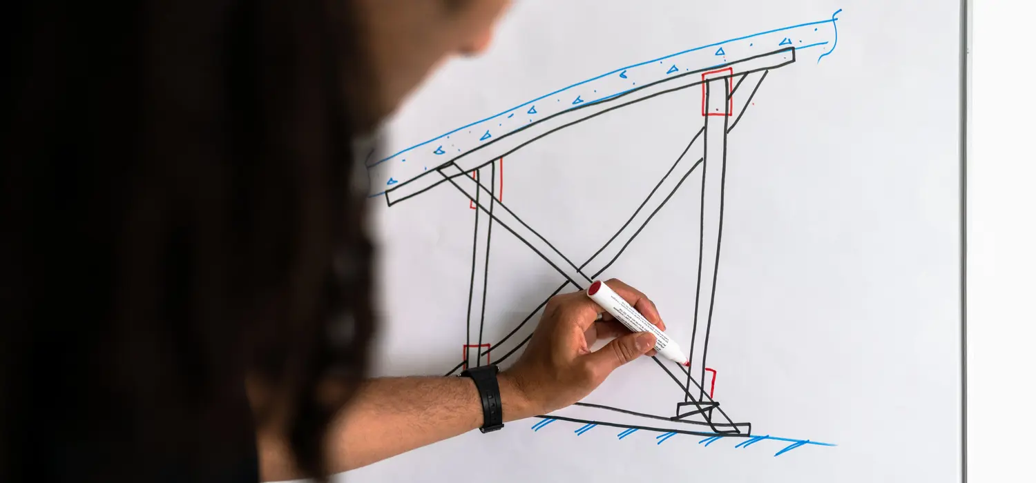 Male structural engineer draws on whiteboard.