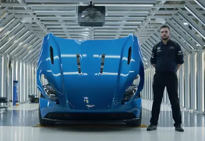 Todd Downs: male manufacturing engineering apprentice in dark coloured uniform standing to the side of a blue Aston Martin with its bonnet open